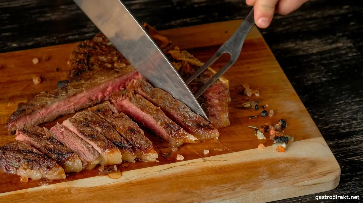 Ein Steak wird auf einem Schneidbrett mit einem Messer zerteilt